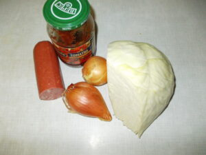Порежьте колбасу секторами, толщиной в 1 см и добавьте в подрумяненный лук. Жарьте до подрумянивания колбасы